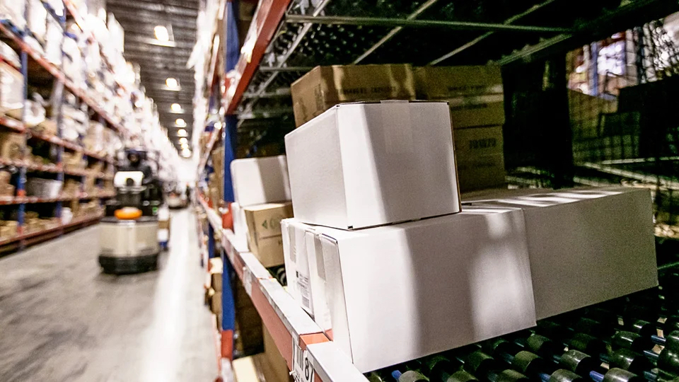 A warehouse interior filled with shelves stacked with boxes and pallets, showcasing organized storage space. FlexMation.