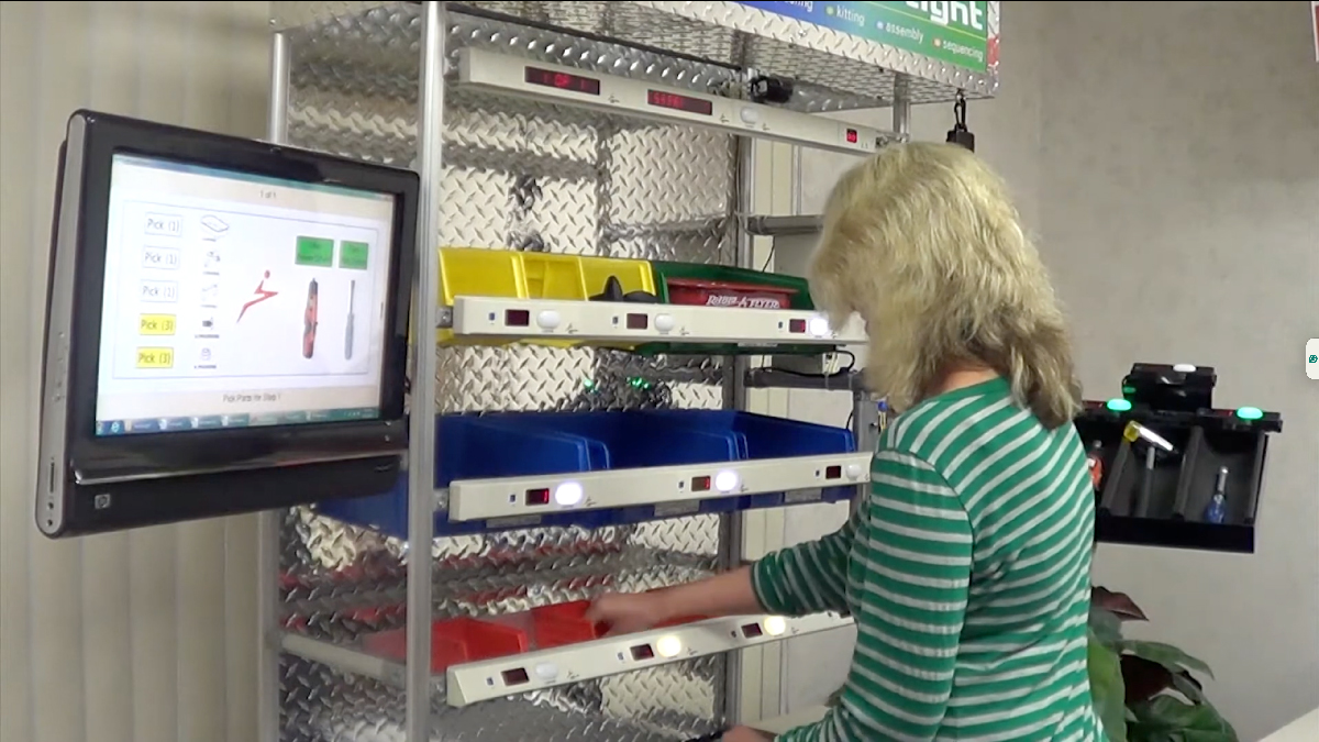 Operator picking items from color-coded bins using a light-guided order picking system with digital interface and flow rack setup