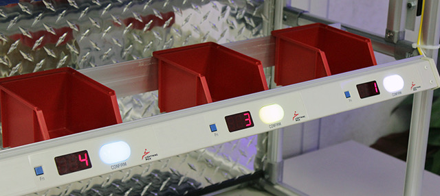 Four red bins on a metal shelf with digital displays below each showing numbers 4, 3, and 1. The shelf has an industrial, organized feel.