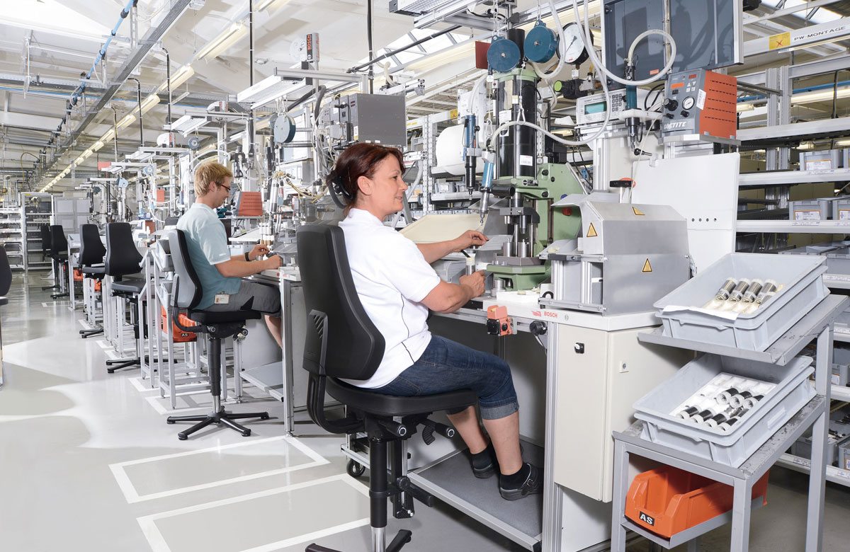 Photo of a room with a lot of machines and customized work stations provided by Flexmation with two people sitting in the special work places.